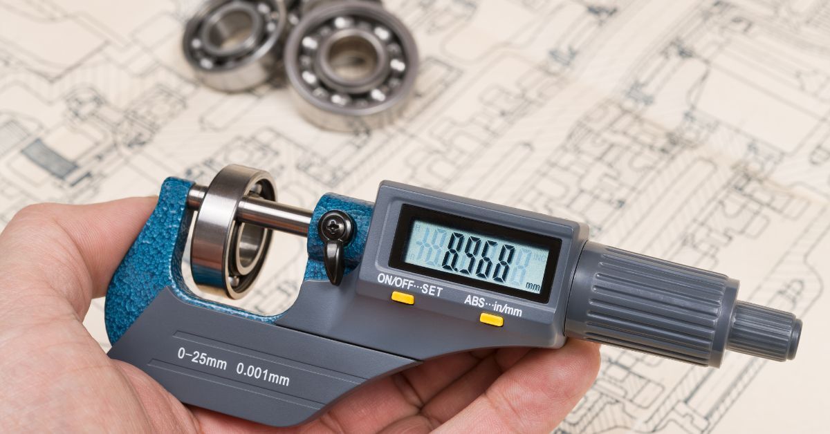 Someone measuring a ball bearing with a micrometer, which reads 8.968. There are more ball bearings on the table behind the tool.