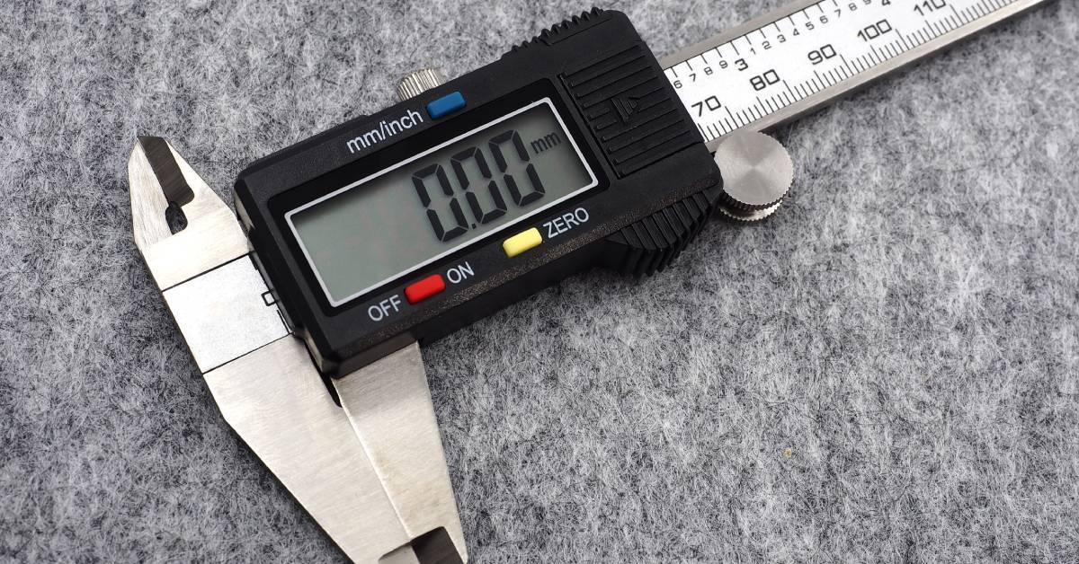 Close-up to a metal digital caliper with a plastic black display with red, blue, and yellow buttons for configuration.