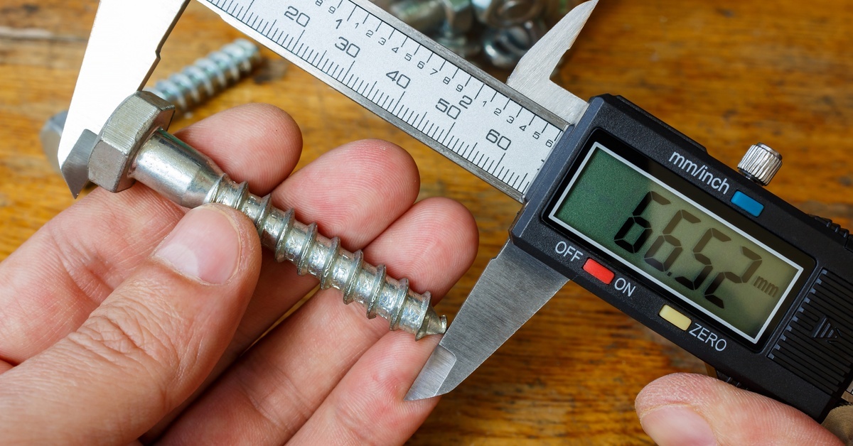 Someone using a digital caliper to measure the length of a screw. The caliper reads 