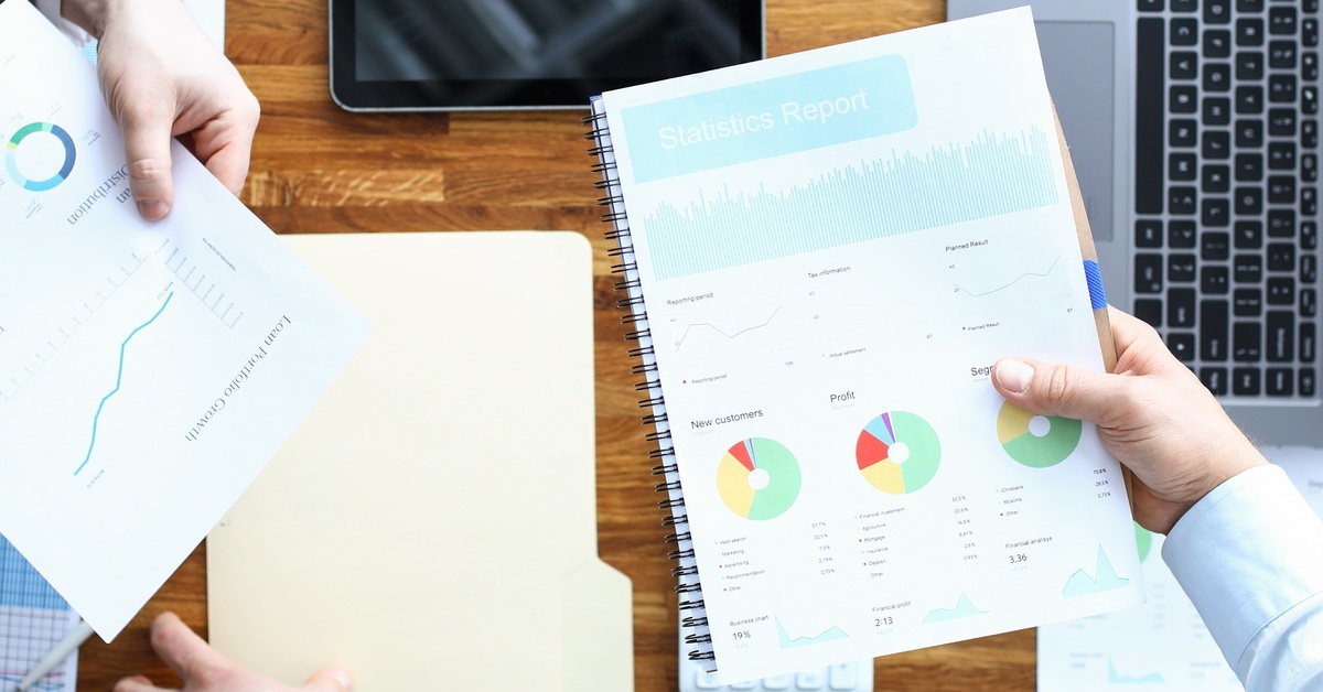 People holding pages showing different types of charts and graphs. They are working at a table with more papers and a laptop.