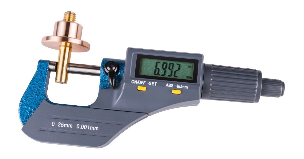 A digital micrometer measuring a small, cylindrical brass piece against a white background. The display reads 6.992 mm.